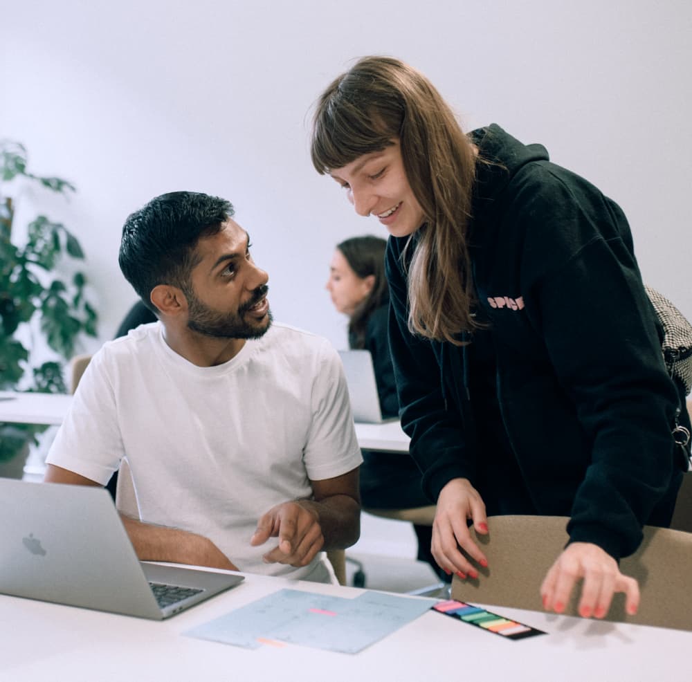 Zwei Personen, die an einem Laptop und Notizen in einem Büro arbeiten.
