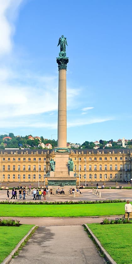 Hoher Säulenmonument mit Statue vor einem Schloss und Menschen.