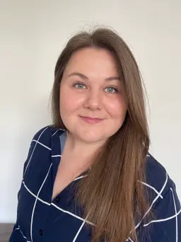 Portrait of a smiling woman with brown hair wearing a blue checkered shirt.