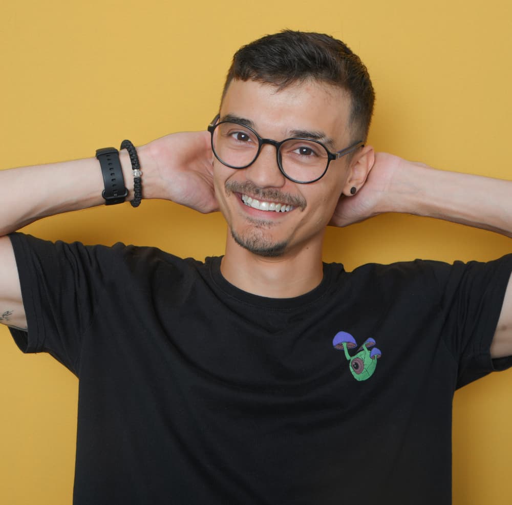 Junger Mann mit Brille vor gelbem Hintergrund lächelnd.