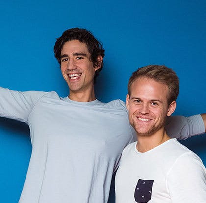 Two men standing next to each other smiling - blue background