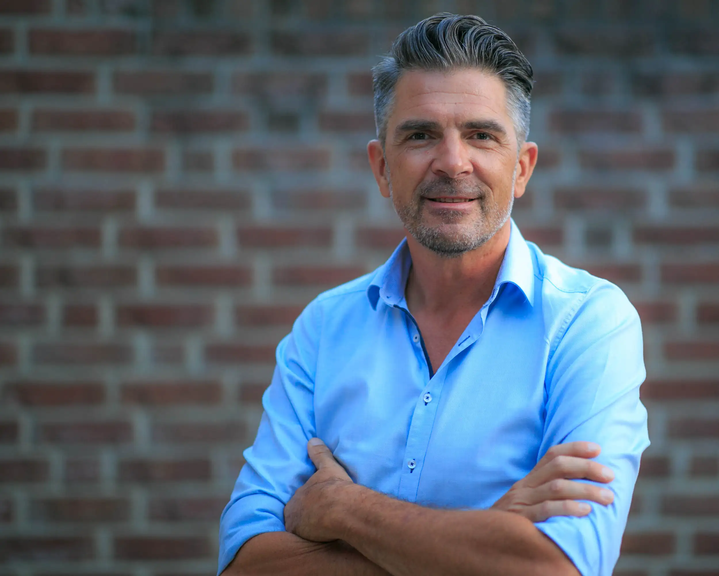 Man with crossed arms in front of brick wall