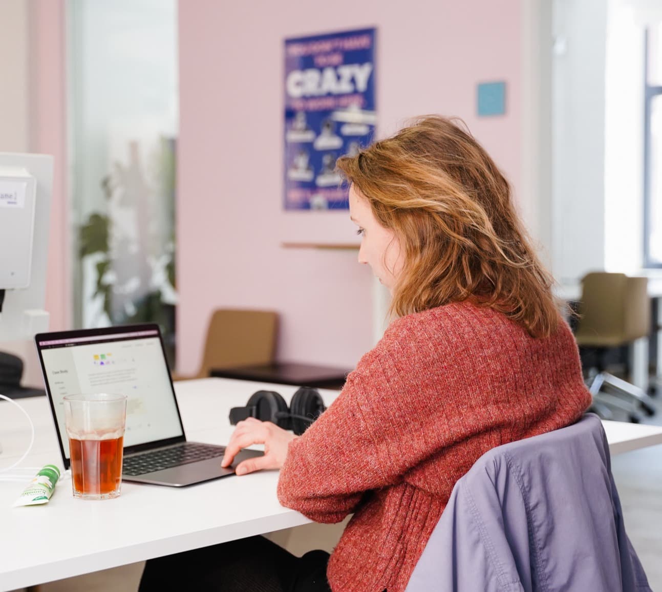 Woman working on laptop in office with a drink.