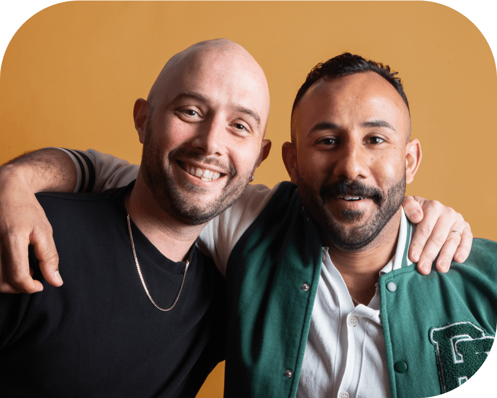 Two smiling men hugging each other against an orange background.