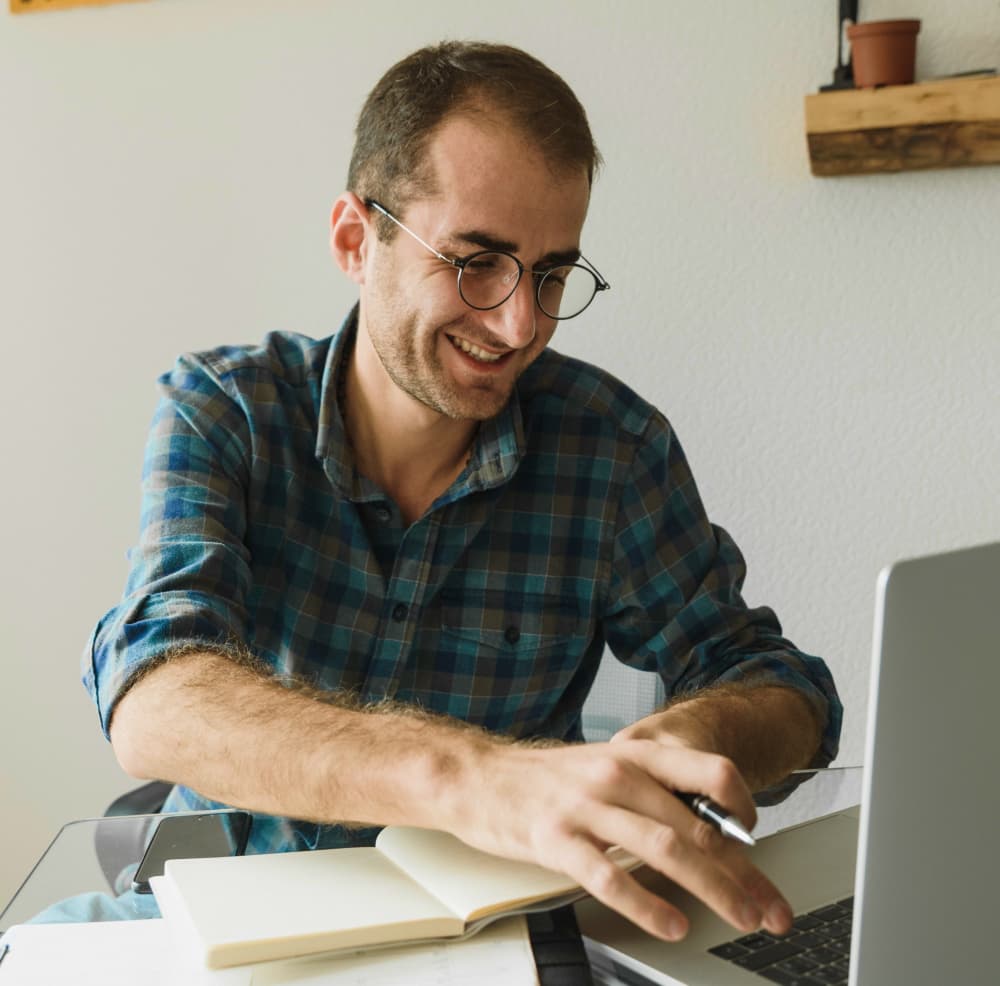 Mann arbeitet am Laptop und schreibt in Notizbuch